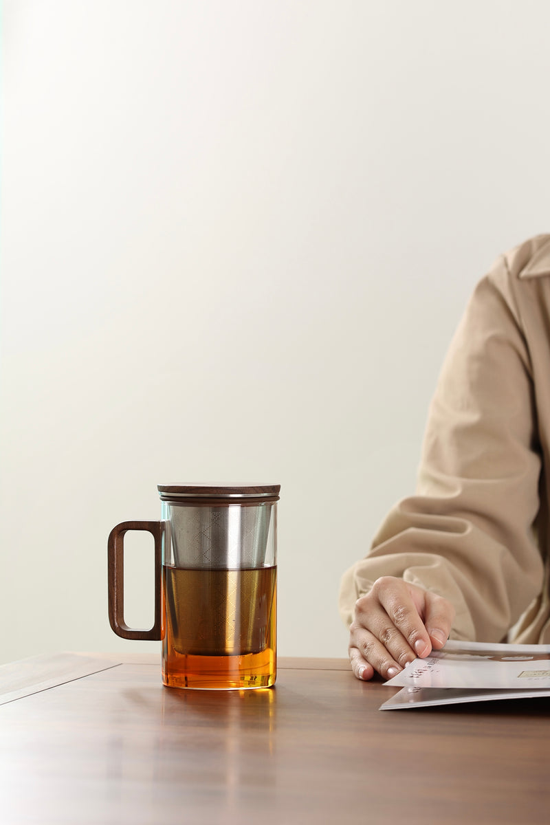 Person sitting at a table with a mug of tea and a newspaper.